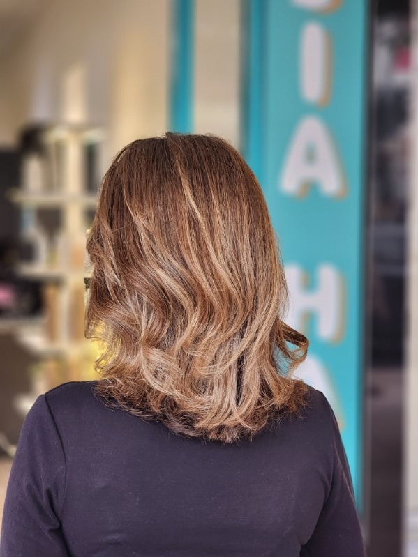 Shoulder-length hair with soft caramel highlights and loose waves, seen from behind at the JIA HAIR entrance